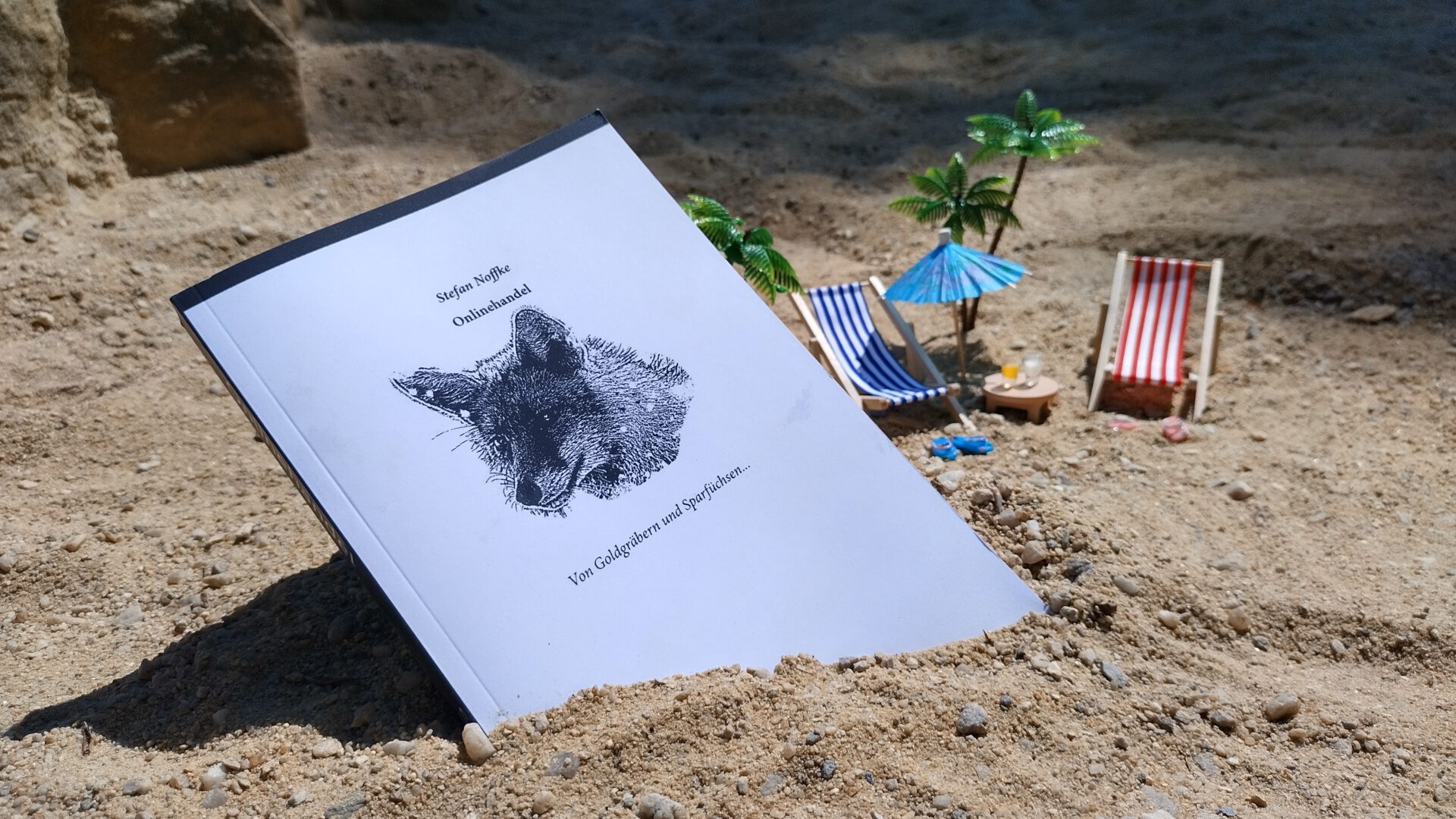 Foto des Buches Onlinehandel am Strand mit Liegestühlen und Sonnenschirm. (Miniaturlandschaft) Sommerferien